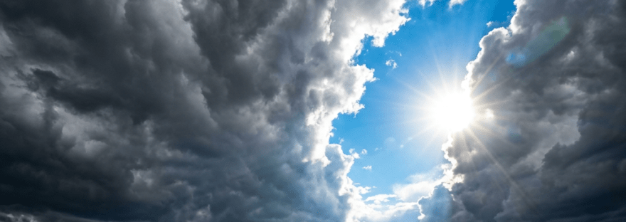 Sun rays shining through dark storm clouds above green and brown mountains